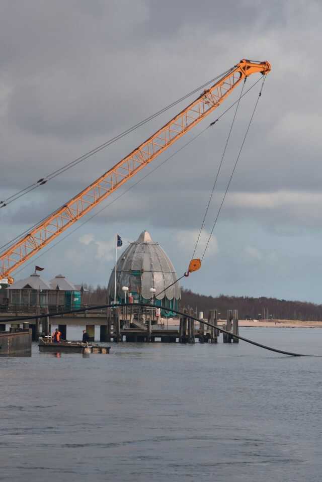Vom Kran des Arbeitsschiffs wird der knapp 400 m lange neue Rohrstrang auf dem Wasser schwimmend vorgehalten. Vom Kran des Arbeitsschiffs wird der knapp 400 m lange neue Rohrstrang auf dem Wasser schwimmend vorgehalten.