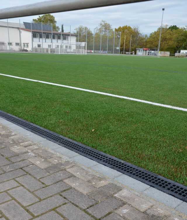 An den Einlaufkästen beginnend, wurden die Rinnenstränge entlang des Spielfeldrandes auf ein Betonfundament gesetzt und mit einer Rückenstütze aus Beton stabilisiert. An den Einlaufkästen beginnend, wurden die Rinnenstränge entlang des Spielfeldrandes auf ein Betonfundament gesetzt und mit einer Rückenstütze aus Beton stabilisiert.