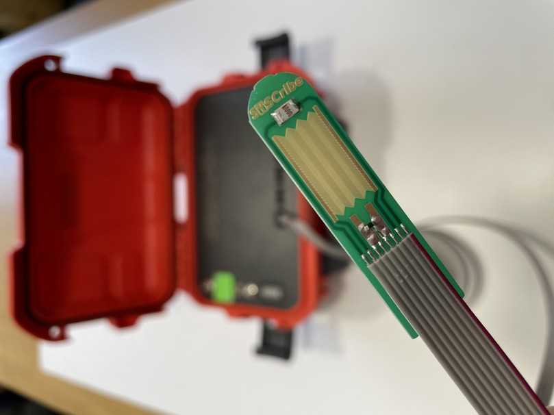 Der fingergroße, ca. 1 mm dicke Sensorkopf von Syscribe misst Temperatur, Lichtintensität und elektr. Widerstand/Impedanz. Im Hintergrund die rote Messbox mit der Messtechnik und Sendereinheit. | Foto: Syscribe Der fingergroße, ca. 1 mm dicke Sensorkopf von Syscribe misst Temperatur, Lichtintensität und elektr. Widerstand/Impedanz. Im Hintergrund die rote Messbox mit der Messtechnik und Sendereinheit. | Foto: Syscribe